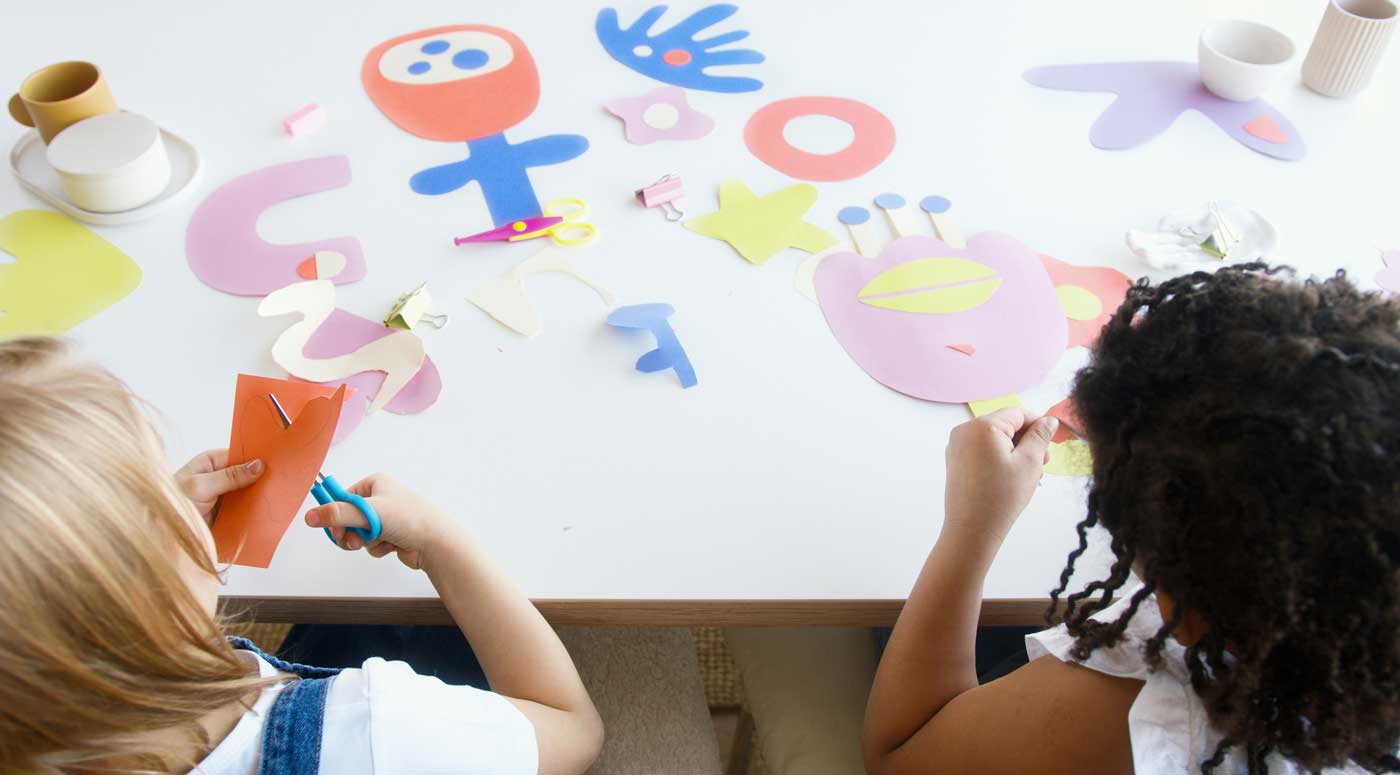 blick von oben, zwei kinder sitzen am tisch und basteln